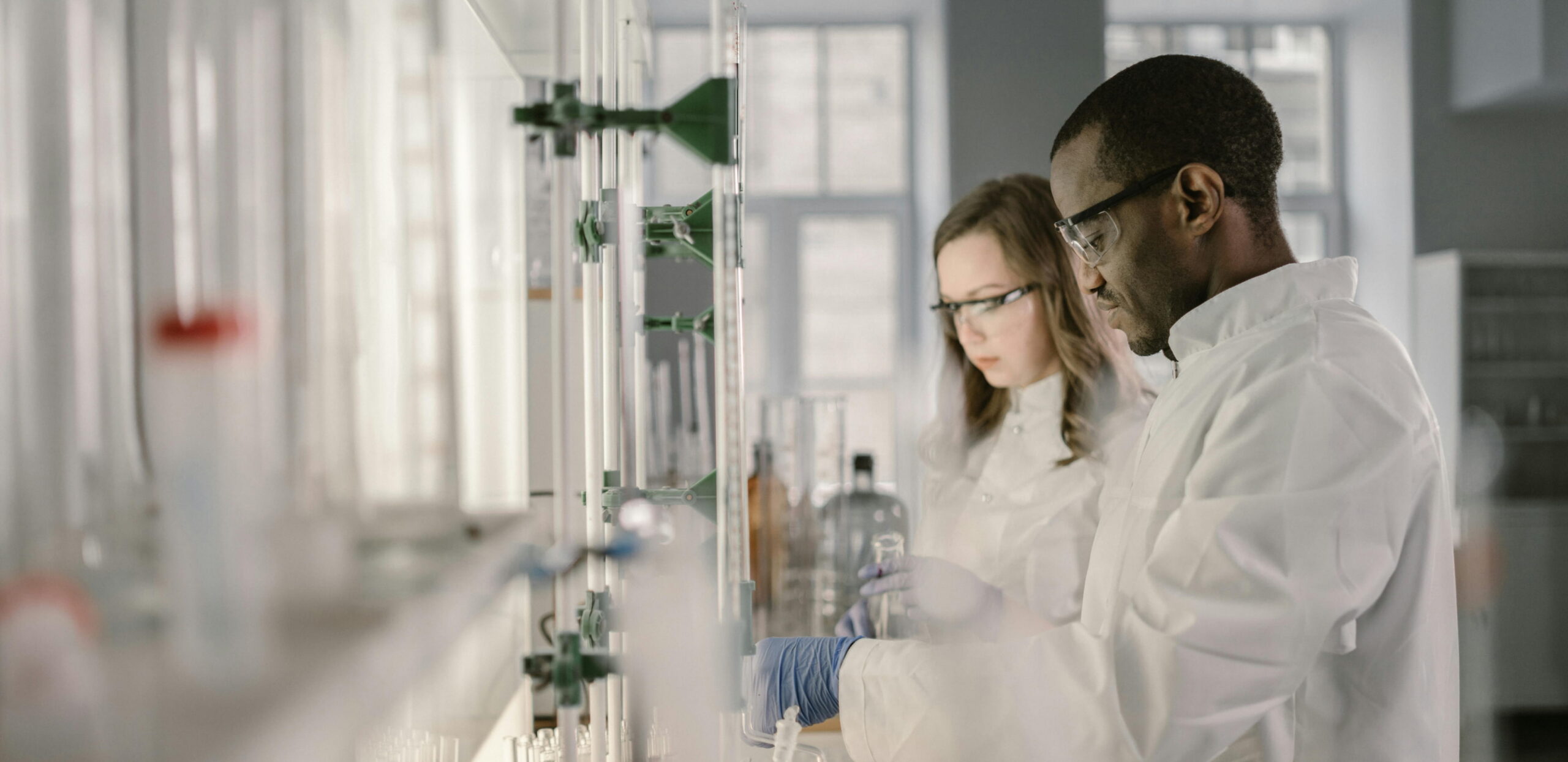 Two scientists in lab coats and safety goggles working with glassware in a laboratory