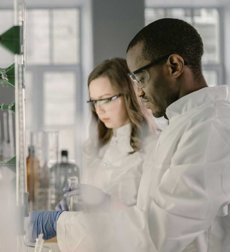 Two scientists in lab coats and safety glasses working with equipment in a laboratory